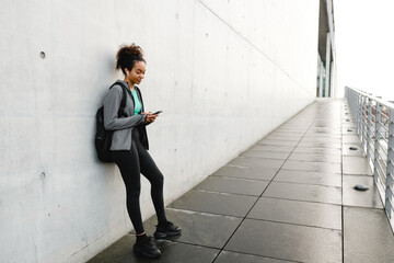 Fototapeta premium African girl listening music with earphones and mobile phone while standing outdoors over gray wall