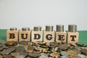 Rosnący stos monet na drewnianych klockach z napisem budget. pomysł na budżet inwestycyjny i budżet roczny. Rozsypane luzem monety, - obrazy, fototapety, plakaty