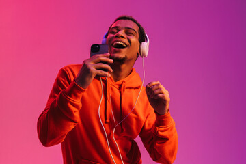 African man listening music with headphones and singing while holding smartphone like microphone...