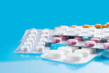 Pile of various pills and tablets in a blister packs on blue background, healthcare and medicine concept
