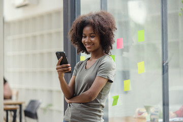 Happy Young African American Woman Using Mobile Phone In Hands And Standing At Office,  