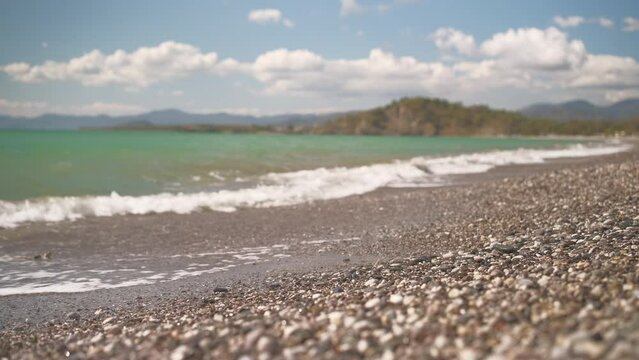 View of the bay and summer sky on a pebble beach in the Aegean Sea, 4k live video, selective focus, beautiful footage of sea waves washing the beach during vacation