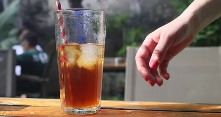 A female hand picks up a glass of iced tea on a hot summer day. - Powered by Adobe