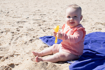 Baby girl playing in the sand with plastic toy. 8 months old baby with blonde hair at the beach.