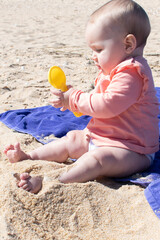 Baby girl playing in the sand with plastic toy. 8 months old baby with blonde hair at the beach.