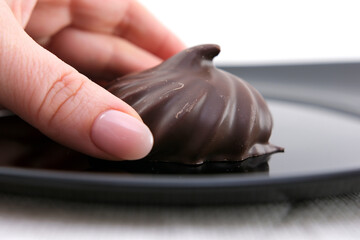 Delicious chocolate covered marshmallow isolated on white. a woman's hand takes a marshmallow in chocolate from a black plate High quality photo