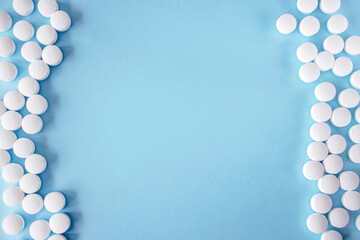 Lots of white pills on a blue background around the edges. Copy space for text. Nutritional supplements and medications.