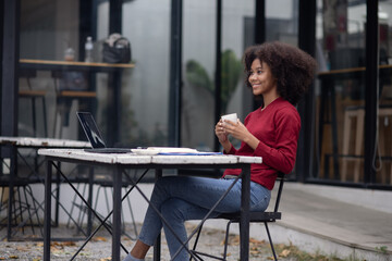 Young African American businesswoman with laptop sitting at table outdoor.