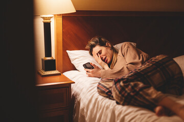 Young depressed woman using mobile phone crying on bed at night feeling sad and depressed victim of...