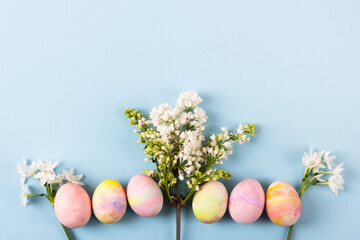 Colorful Easter eggs with spring blooming daffodils and white lilac on a blue background. Happy Easter concept.