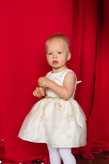 Fototapeta na wymiar beautiful little toddler girl in a red dress against the background of red curtains. Birthday, new year, merry christmas 