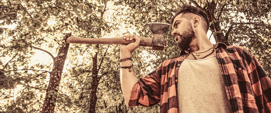 Lumberjack man. Chopping wood. Brutal lumberjack bearded man in woods on a background of trees. Bearded lumberjack with a large ax