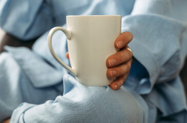 A woman has a white cup of tea or coffee on her knee.