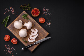 Fresh raw champignon mushrooms on a wooden cutting board with spices