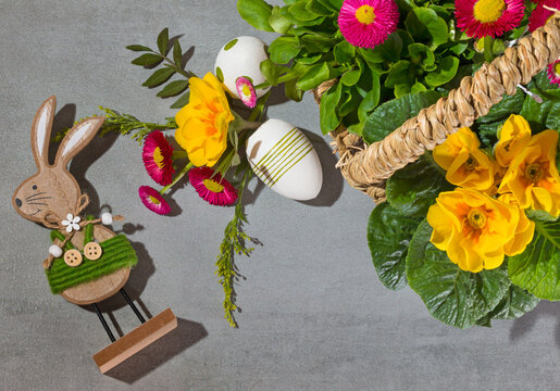 Easter rebbit and Easter eggs with spring flowers in a wicker basket on light gray background.