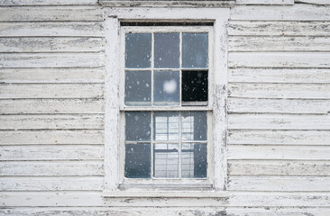 Old house exterior with old wooden boards and broken window. White painted wood siding with antique finish. Snow falling
