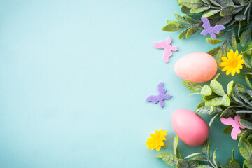 Easter background or greeting card on blue. Eggs, spring leaves, flowers and colored butterflies. Flat lay with copy space.