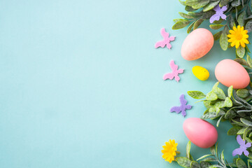 Spring or Easter background on blue. Eggs, spring leaves, flowers and colored butterflies. Flat lay with copy space.