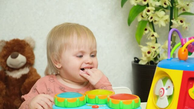 A one-and-a-half-year-old girl sucks her fingers on her hand playing with toys.