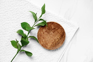 Flat lay cosmetic product presentation scene made with wooden pedestal and green leaves on white towel.