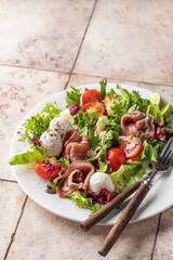 Fresh salad with Prosciutto, salad mix, cherry tomatoes, mozzarella cheese on pink tile background. Healthy food, keto diet, diet lunch concept