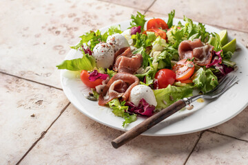 Fresh salad with Prosciutto, salad mix, cherry tomatoes, mozzarella cheese on pink tile background. Healthy food, keto diet, diet lunch concept