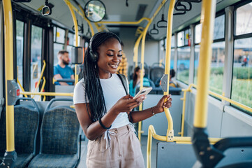 African american woman riding in a bus and using a smartphoneand headphones