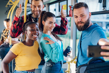 Multiracial friends taking selfie with a smartphone while riding a bus in the city