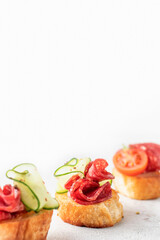 Bruschetta with sausage and vegetables on light gray background. Three of salami sandwiches as appetizer isolated with copy space