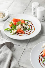 Healthy vegetable salad with fresh arugula, tomato, feta cheese on white plate, gray tile background. Diet menu with text space