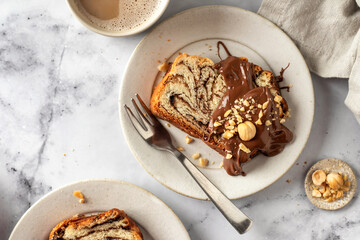 Slice of brioche babka bread with chocolate filling on white marble background served with chocolate and nuts and a cup of coffee. Easter traditional baking top view