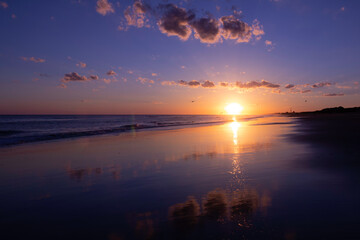 Incredible sunset on the beach. The sun is reflected in the water like a mirror. Tranquil vacation scenery.