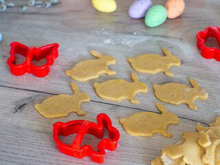 Close-up kneaded ginger dough and carved figurines from it. The shapes of rabbit. Cutting sugar cookie dough with Easter shaped cookie cutters. Preparation for Easter. Holidays baking.