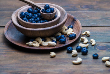 Obraz na płótnie Canvas wood spoon ripe sweet blueberry bowl on dark rustic wooden table. cashew nuts Fresh blueberries background with copy space Vegan vegetarian concept. Delicious Fresh Close up antioxidant fruit.