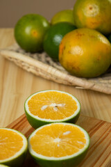 Laranjas cortadas no meio e laranjas inteiras ao fundo em cima de tábua de madeira e mesa de madeira e pano com estampa de folhas
