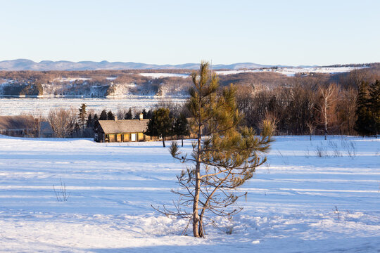 Winter landscape with boarded up chicken coop in field seen in the early morning, with the St. Lawrence River and Laurentian mountains in the background, Beaumont, Bellechasse County, Quebec, Canada
