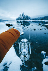 Photo of woman's hand holding an old-fashioned lantern with a background of snowy island in the middle Lake Wenatchee, first person view.