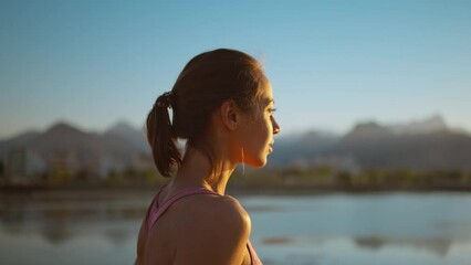 portrait calm confident woman standing on wooden jetty pier, enjoying watching sunset with mountains and sea view. woman relaxing after evening workout, breathing exercises, yoga and meditation
