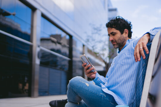 Middle-aged Latin worker taking a break on a city bench while checking his cell phone. Copy space.