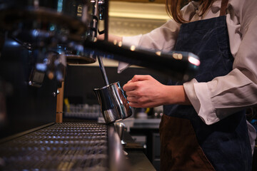 Barista standing next to a coffee machine in a coffee shop and heating up milk.