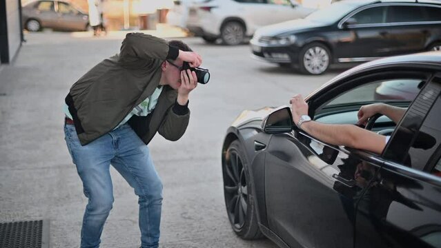 Professional photographer shooting a man posing while sitting in a black car