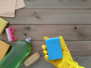 Kitchen sponge in hand. Flat lay. Concept of spring Deep clean of house. Place for text. Rubber glove with washcloth on blurred background of wooden table with cleaning tools. Copy space. Top view.