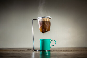 Café quente derramando através de coador de tecido em xícara de cor verde na mesa de madeira.