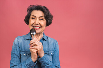 Portrait of senior aged mature woman holding spoon calculating calories meal isolated over pink background.