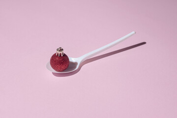 Creative concept made with white spoon and red Christmas decoration. Minimal composition. New Year pastel pink background.