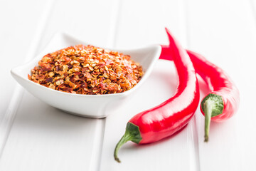 Dry chili pepper flakes. Crushed red peppers in bowl on white table.