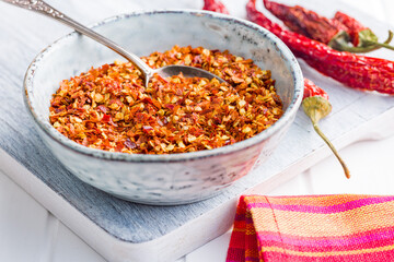 Dry chili pepper flakes. Crushed red peppers in bowl on white table.