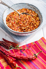 Dry chili pepper flakes. Crushed red peppers in bowl on white table.