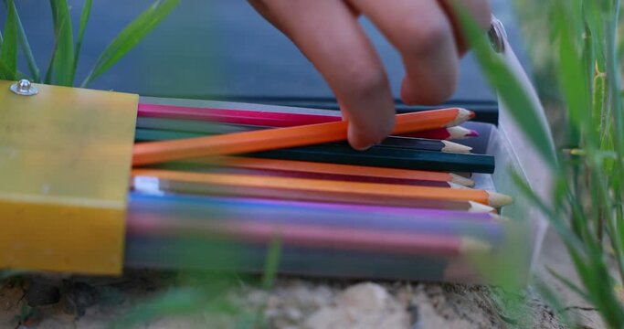 a hand lifting a pencil out of a colorful pencil box