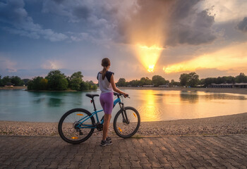 Woman riding a mountain bike near lake at sunset in summer